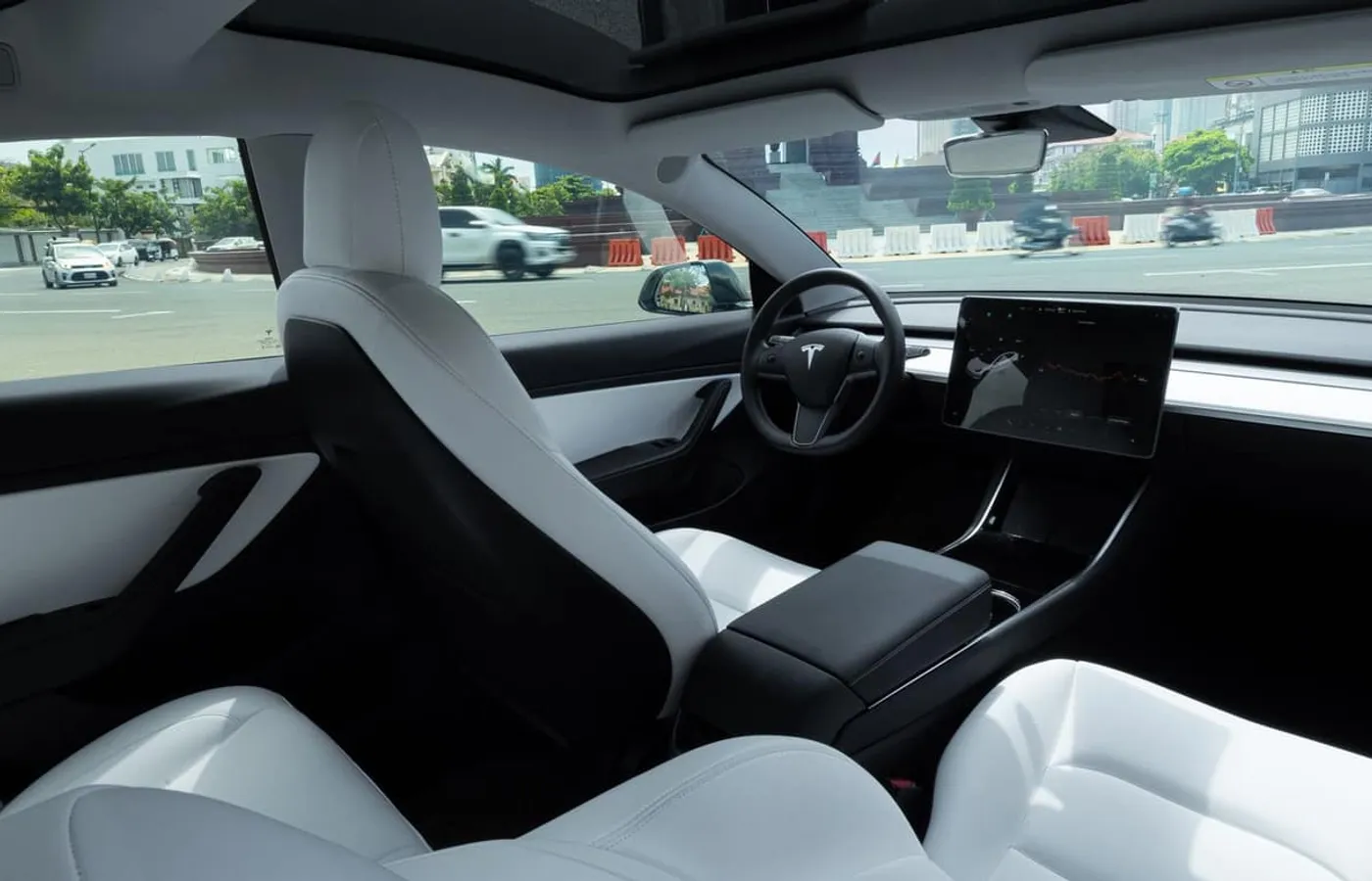 The cabin of a Tesla seen from the rear seats, with white upholstery, the centre console and the centre touchscreen in view