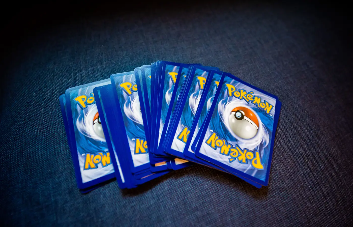 Several fanned stacks of Pokemon trading cards lying face down on dark blue fabric, their blue and yellow backs facing up