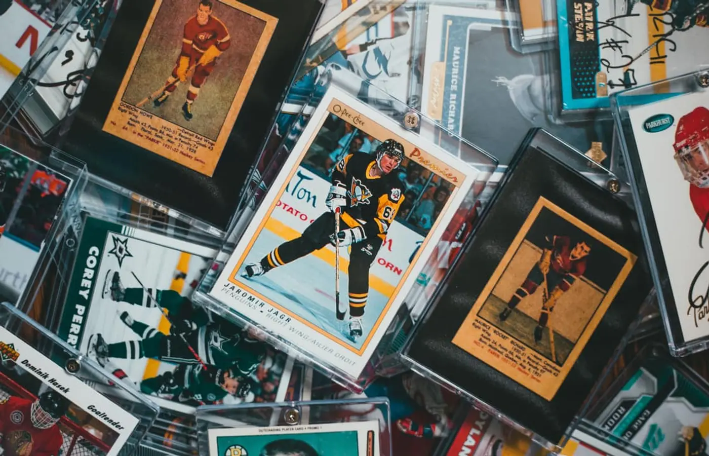 An overlapping pile of vintage and modern sports trading cards, most of them in clear toploaders and magnetic holders, photographed from above